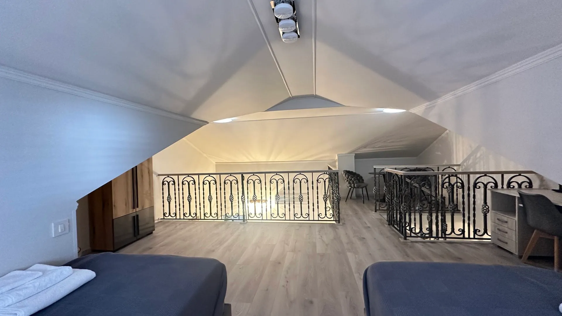 Attic bedroom with two beds, wood flooring, and an ornate wrought iron balcony railing.