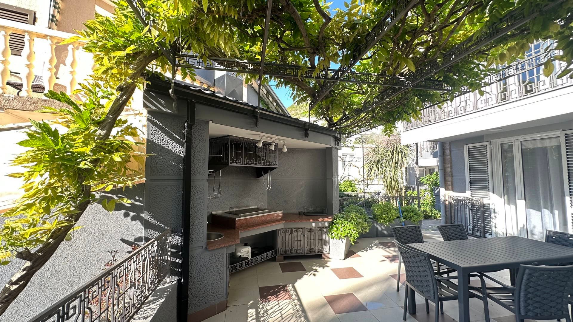 Cozy terrace with a barbecue area and dining table at a hotel in Pržno, Montenegro. Summer patio under a canopy of greenery.