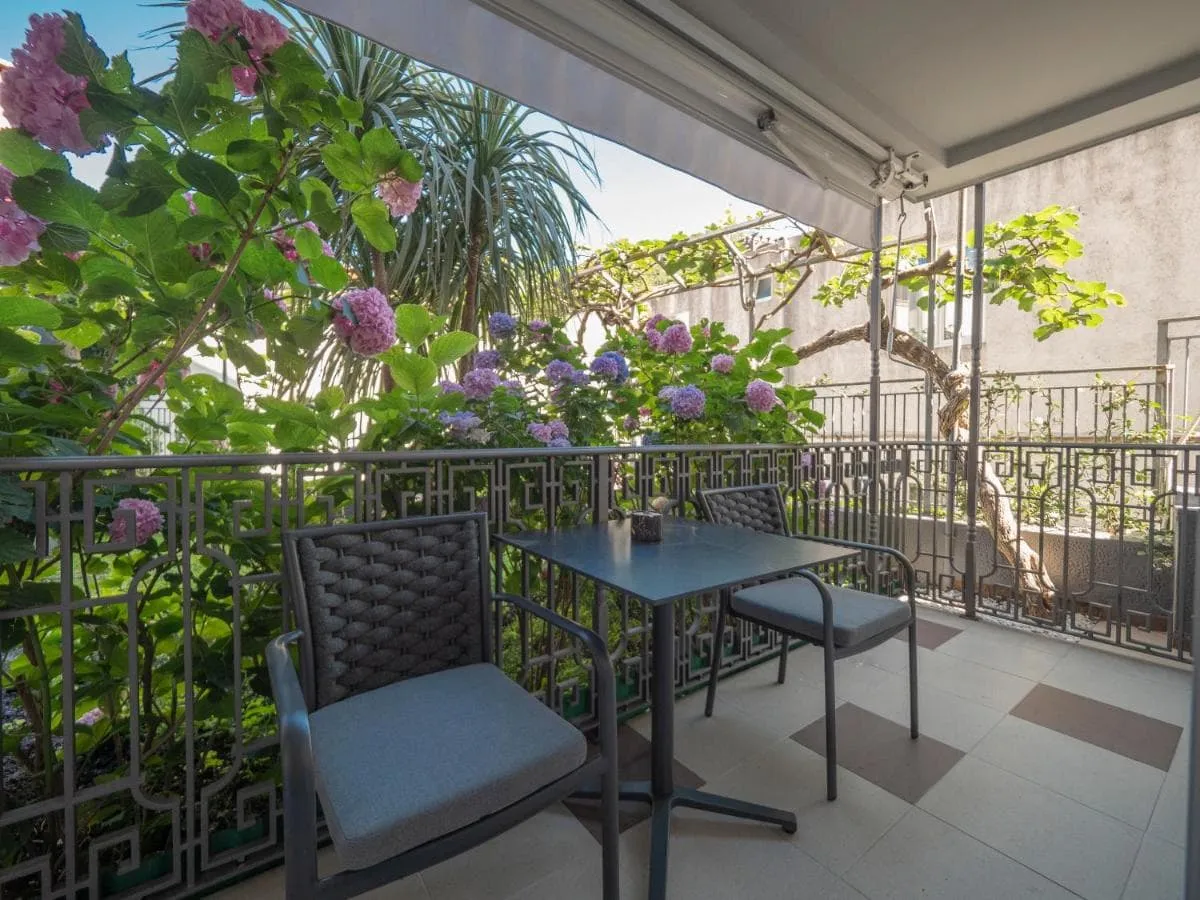 Balcony with metal table and chairs surrounded by blooming hydrangeas behind a decorative railing.