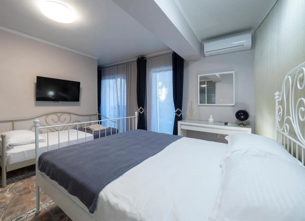 Bedroom featuring two white metal beds, a wall-mounted TV, air conditioner, and a desk with a mirror near the window.