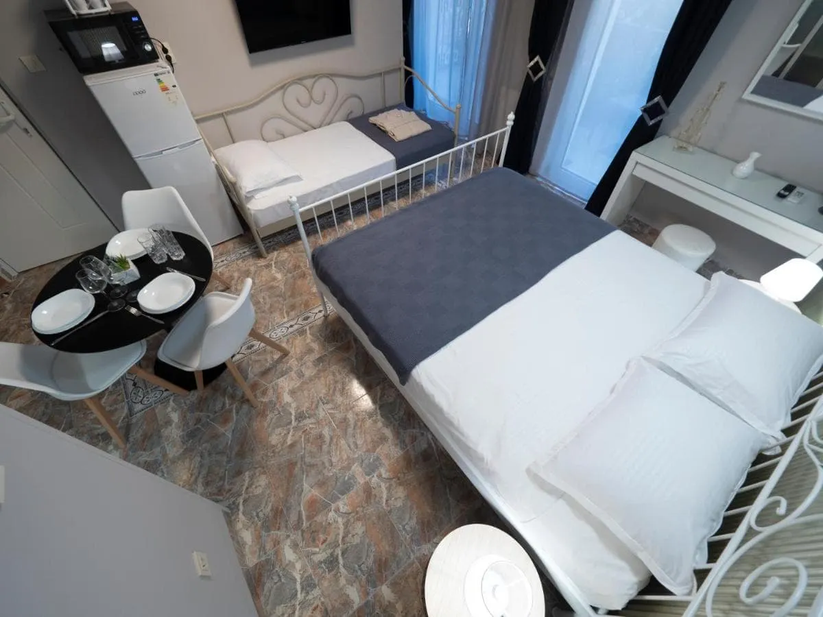 Bedroom with a double bed, single bed, small dining table, and refrigerator in a studio layout.