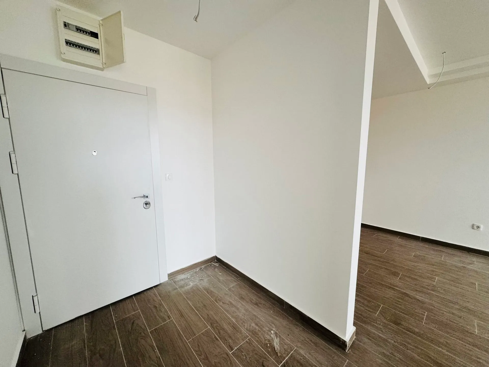 Empty entryway featuring a white door and an open electrical breaker box mounted on the wall above.