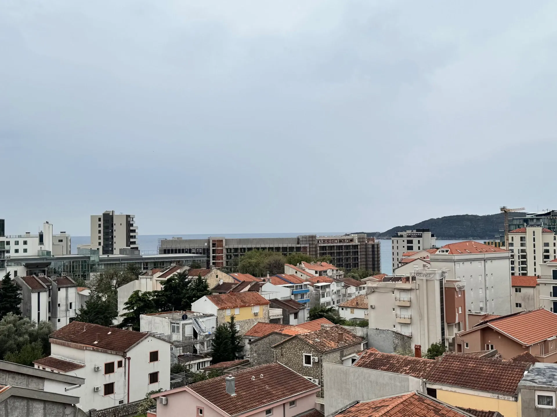 Panoramic view of city rooftops and sea under an overcast sky.