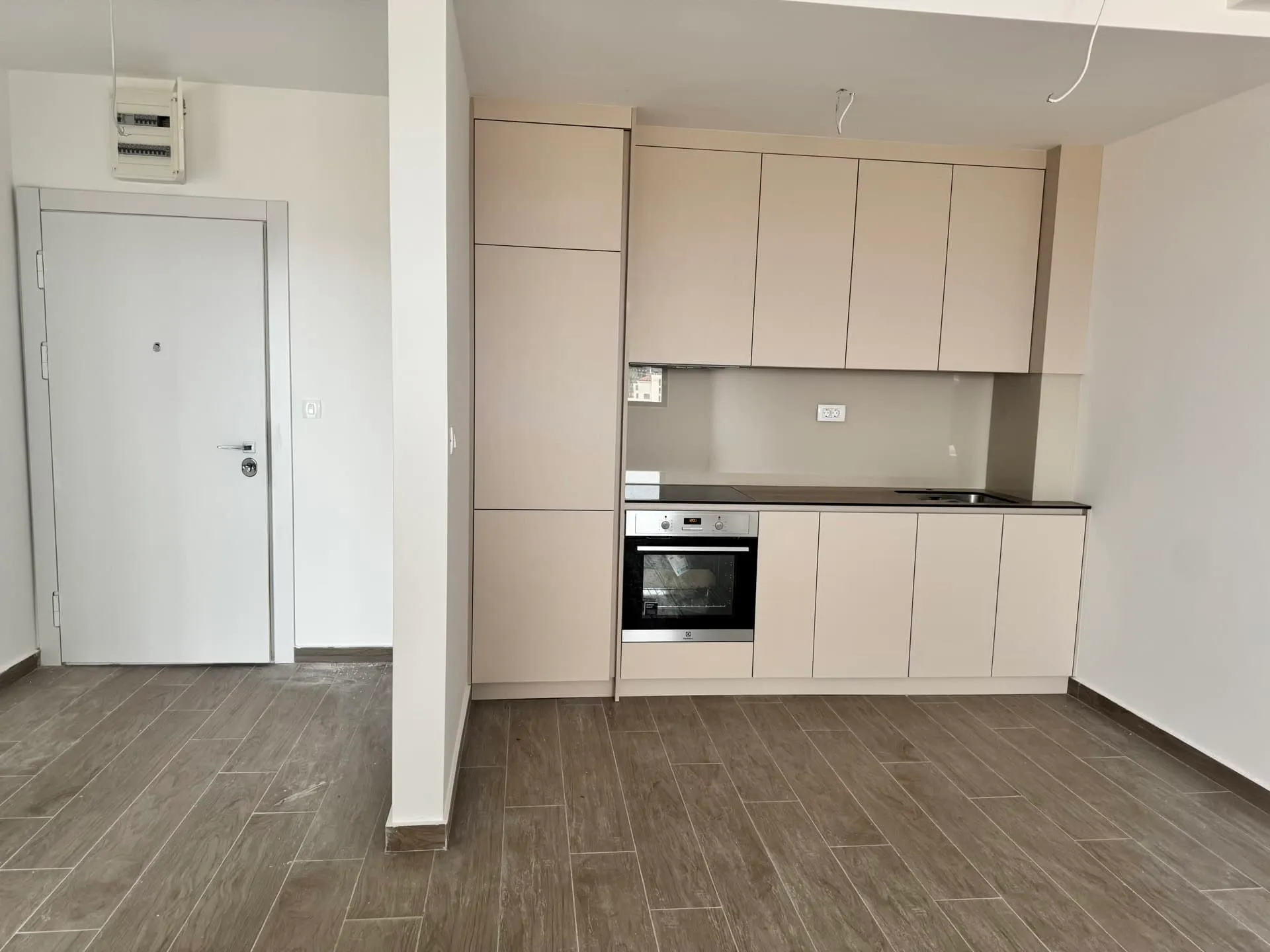 Modern kitchen with beige cabinets, built-in oven, cooktop, and dark countertop next to an entry door.