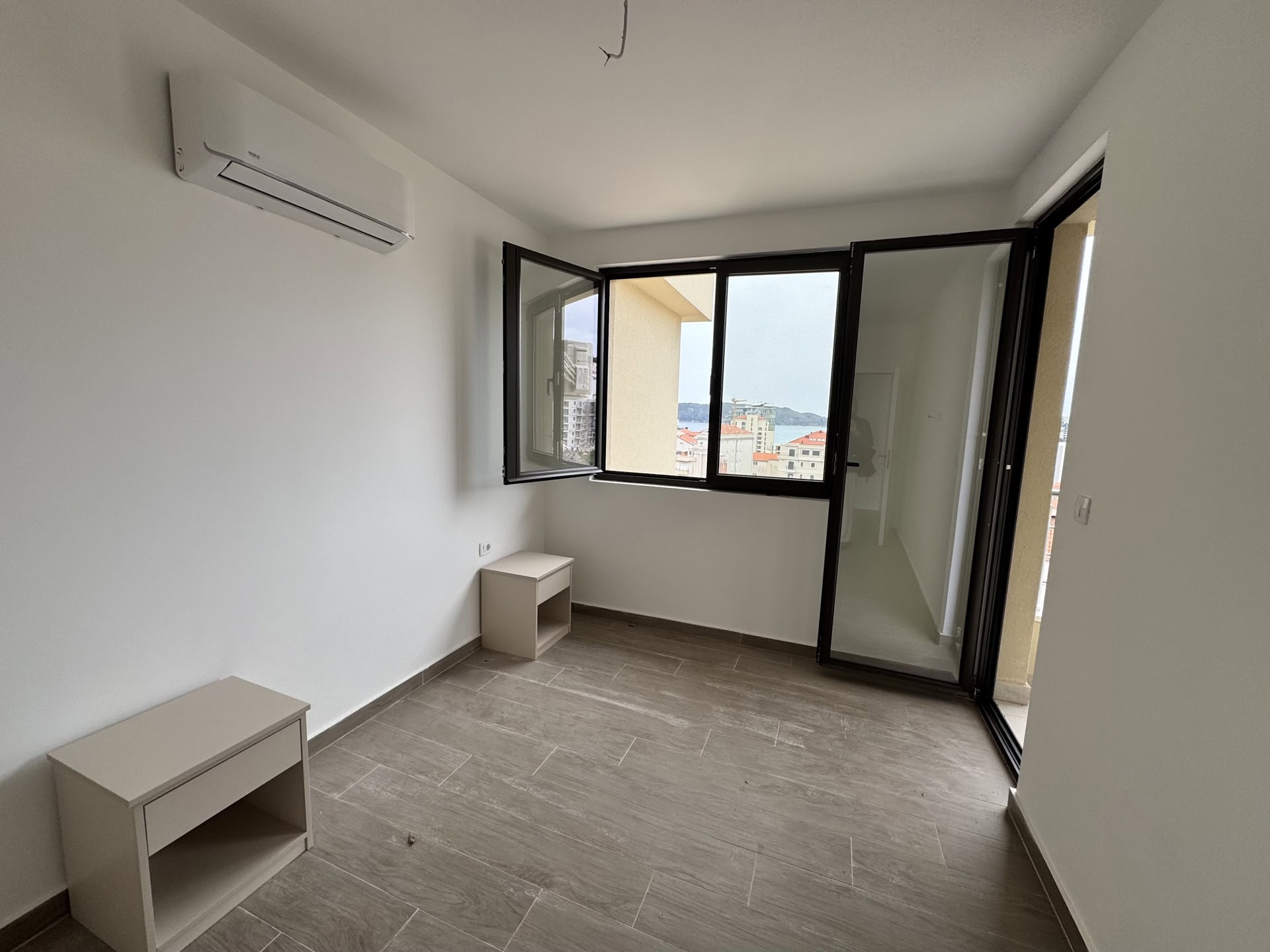 Bright bedroom in an apartment in Bečići, Montenegro: panoramic window with sea view, air conditioner, and tiled floor.