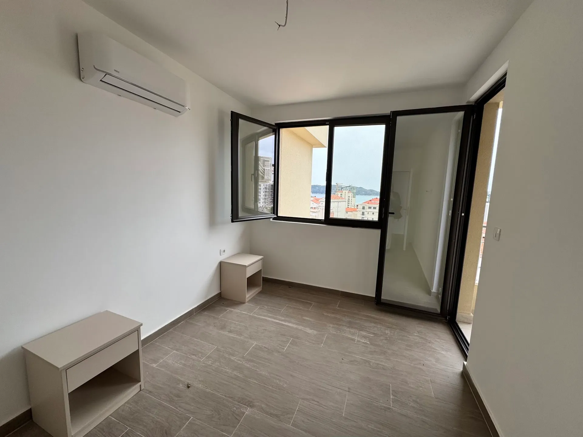 Empty room with grey tile floor, wall AC unit, and two small beige cabinets near white walls.