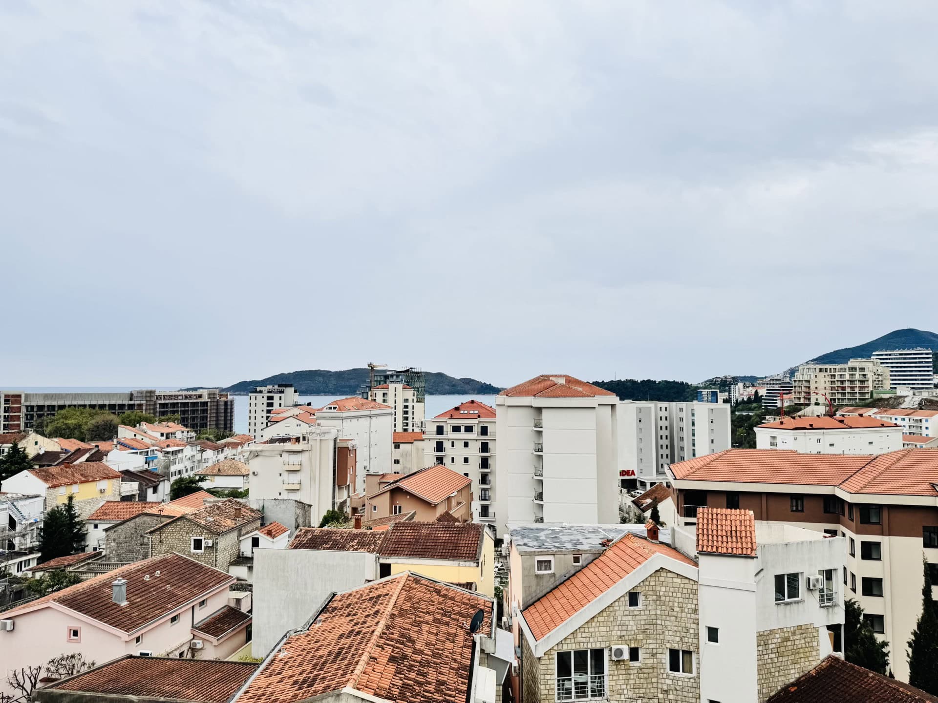 Panoramic view of the city of Bečići, Montenegro, with red-tiled roofs and the sea coast on the horizon.