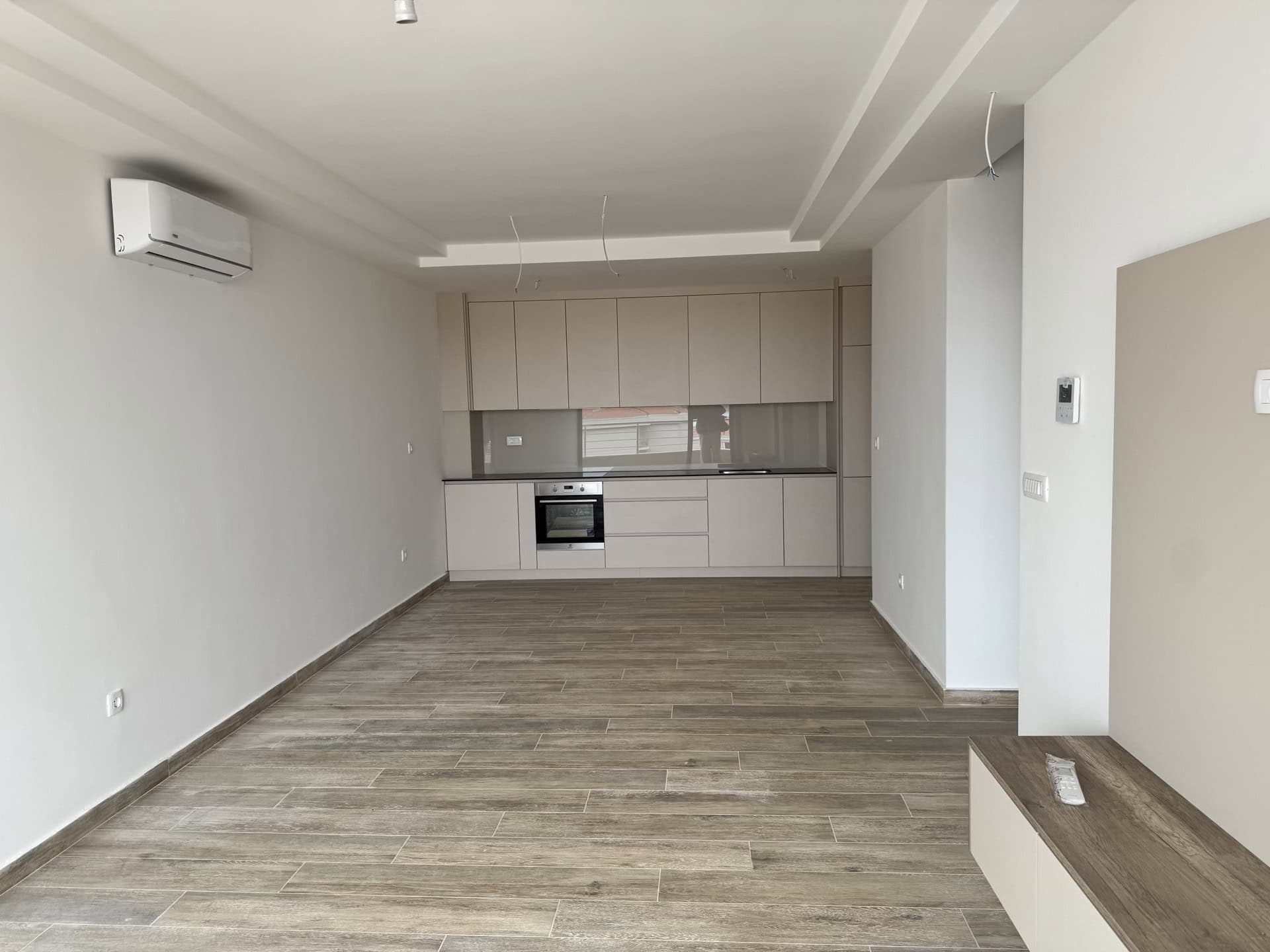 Modern kitchen-living room in a new apartment in Bečići, Montenegro: light-colored cabinetry, built-in appliances, and wood-look tile.