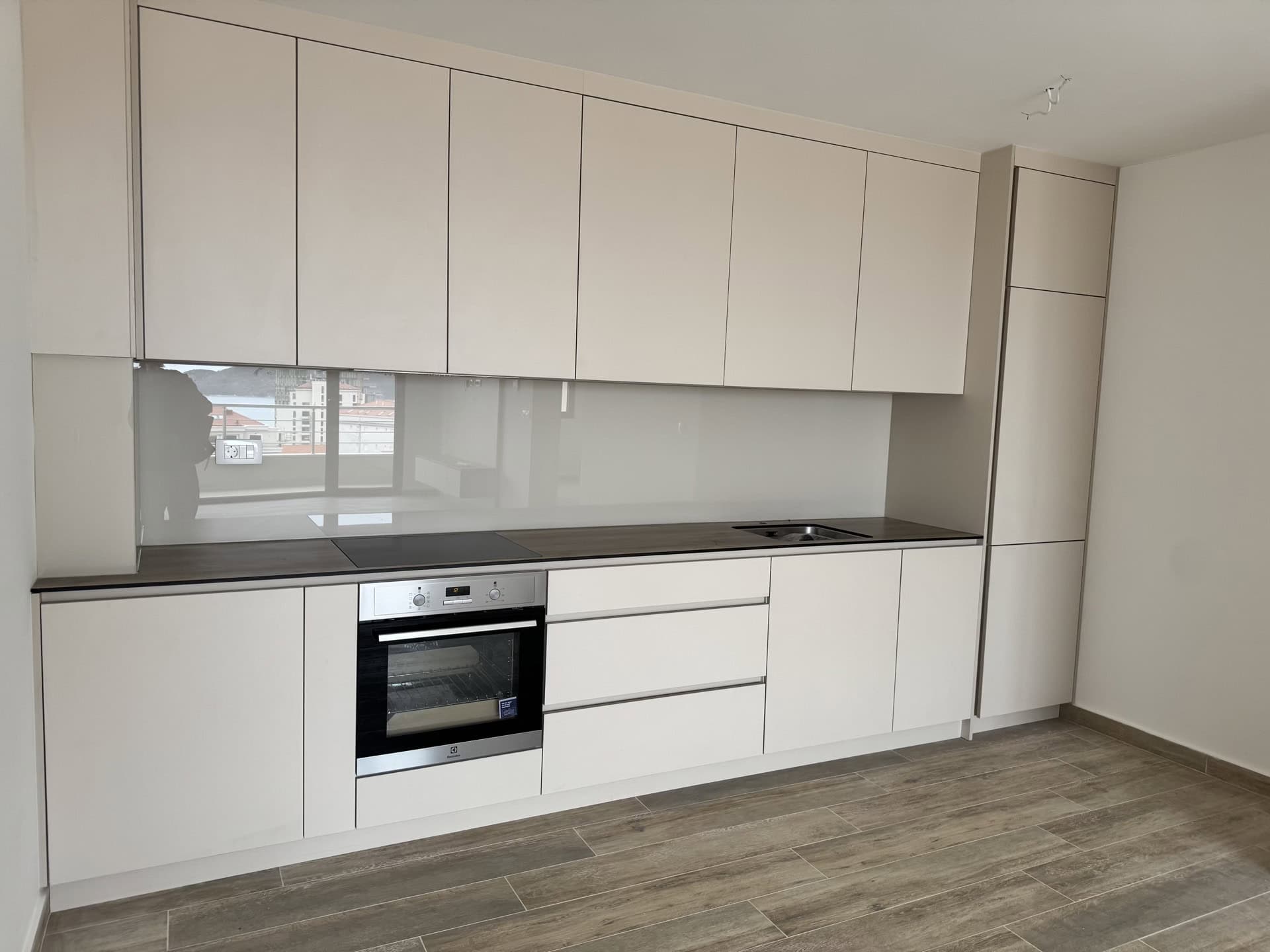 Modern bright kitchen in an apartment in Bečići, Montenegro: built-in appliances, matte fronts, and a view from the window.