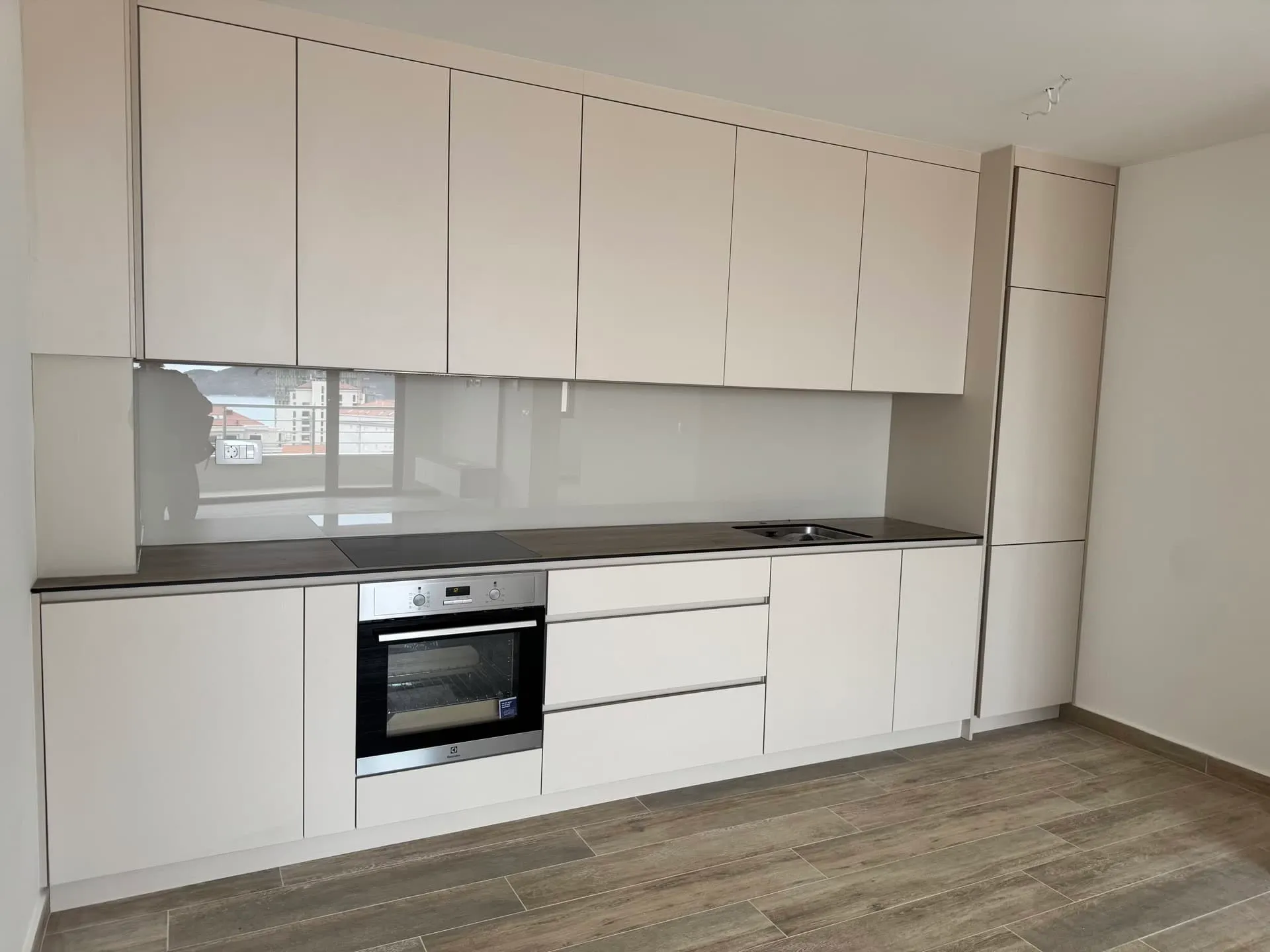 Modern kitchen featuring white cabinets, built-in oven, induction cooktop, sink, and dark countertop with wood-look floor.