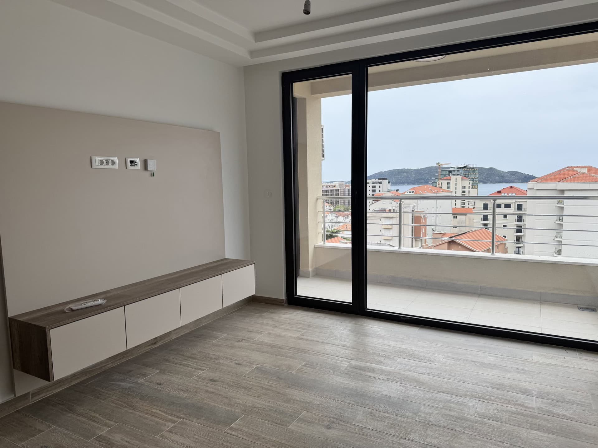 Living room in an apartment in Bečići, Montenegro: modern finishes, a floating TV cabinet, and panoramic sea views from the balcony.