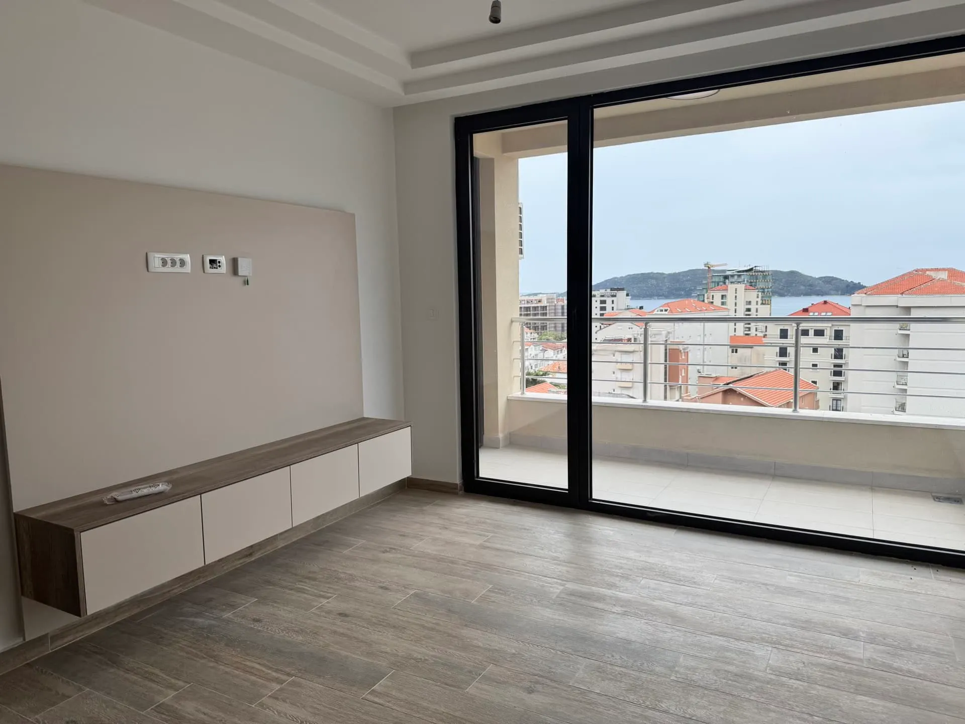 Empty room with wood-look tile and floating media console, featuring large sliding glass doors to a balcony.