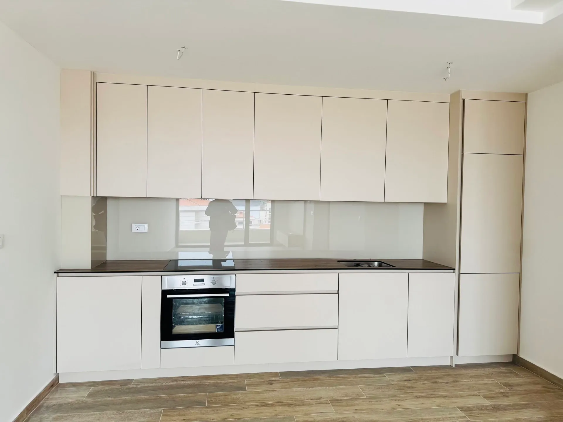 Modern kitchen with white cabinets, dark countertop, built-in oven, sink, and light wood-look tile flooring.