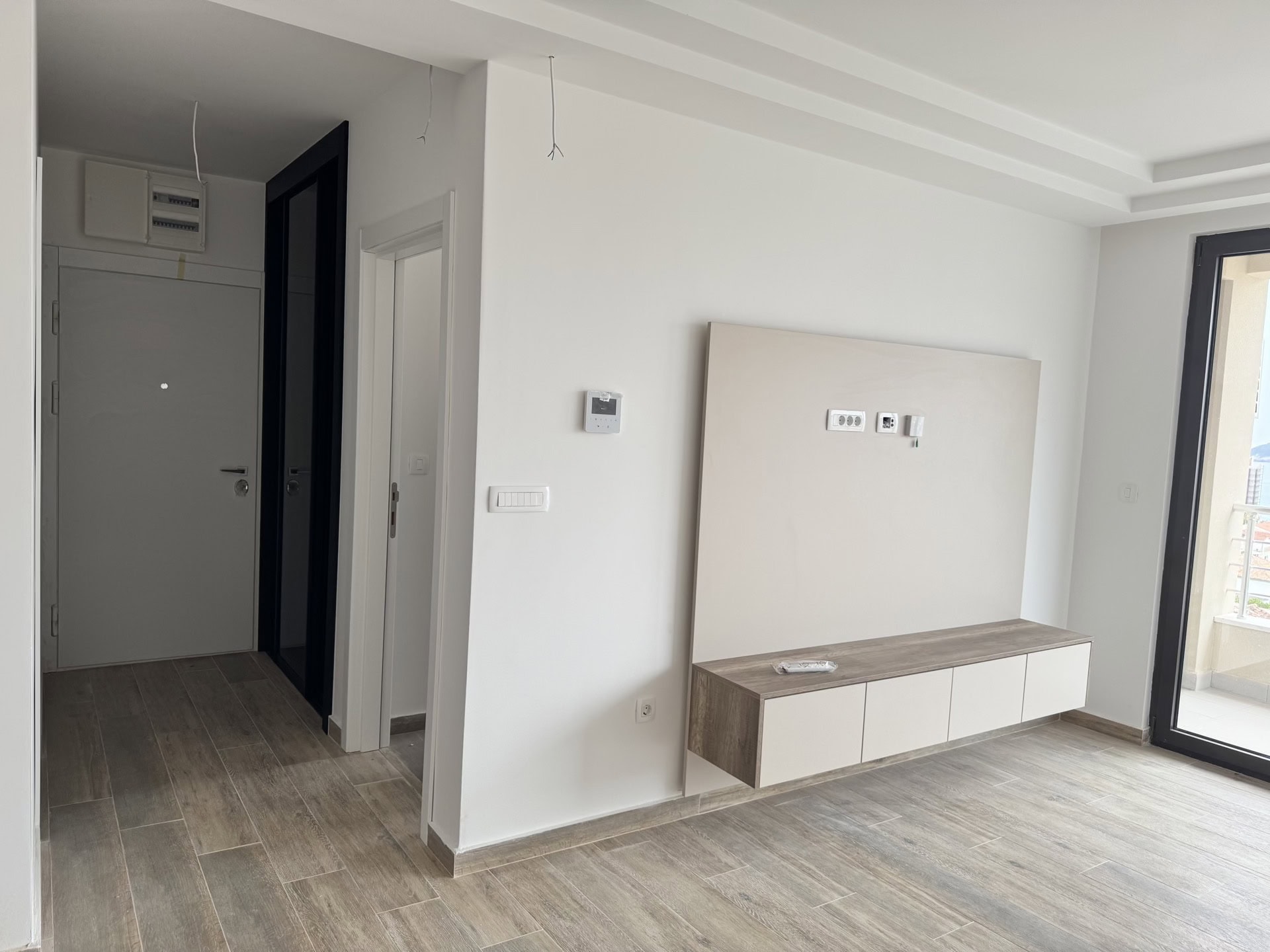 Modern living room in a new apartment in Bečići, Montenegro: wall-mounted TV cabinet, light finishes, and access to the balcony.