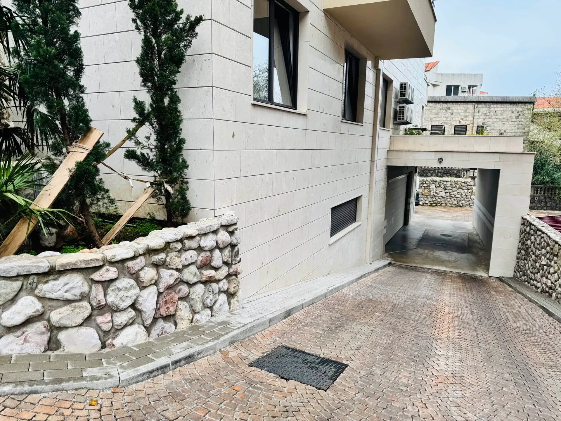 House exterior with stone wall, paved driveway, and garage entrance under a bright sky.