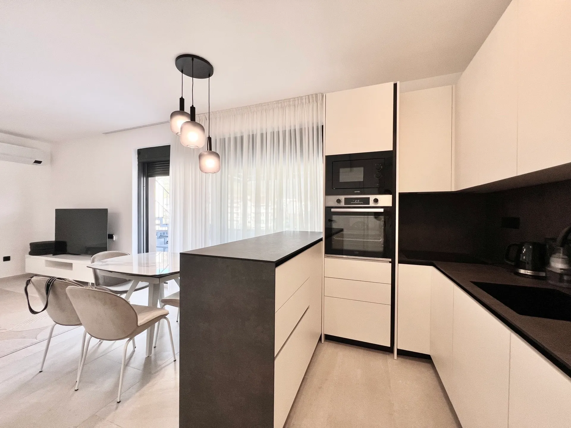Modern kitchen with white cabinets, black countertops, island, built-in appliances, and a dining area visible in the background.