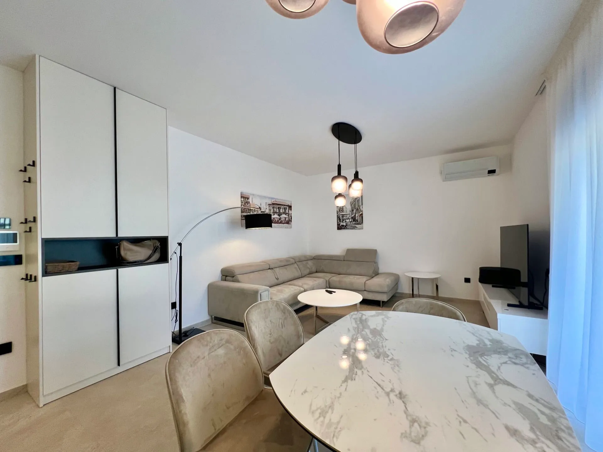 Modern living room featuring a gray sectional sofa, marble dining table, and white storage cabinets.