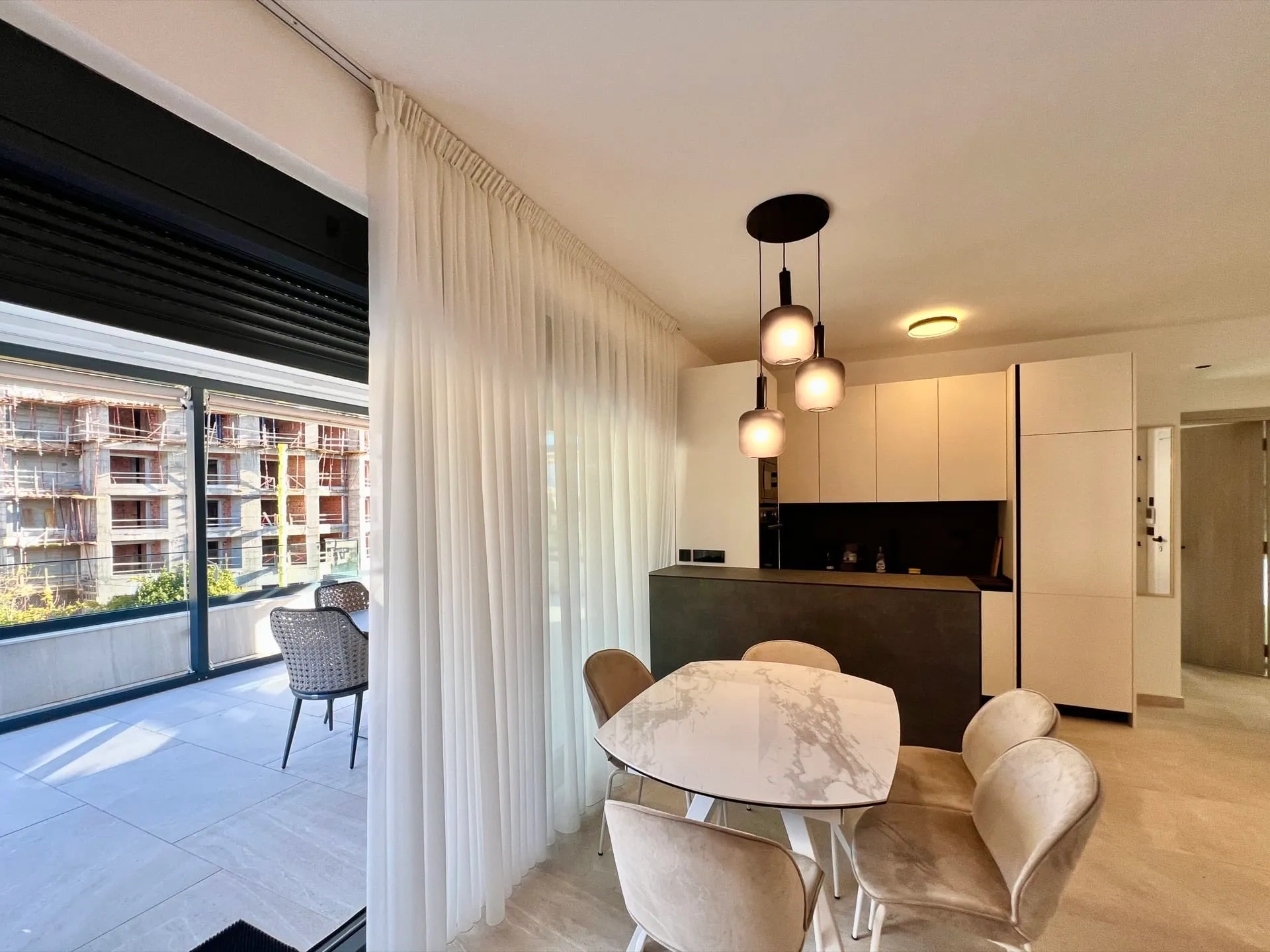 Modern dining area with a marble table and kitchen island adjacent to a balcony.