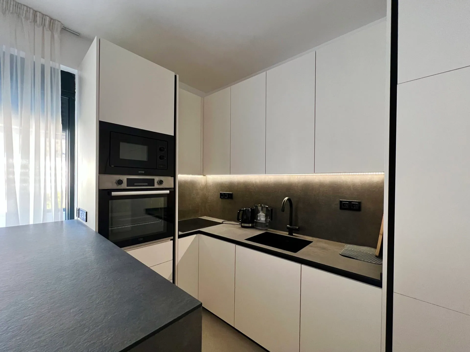 Modern kitchen with white cabinets, black sink, built-in oven, microwave, and dark countertop.