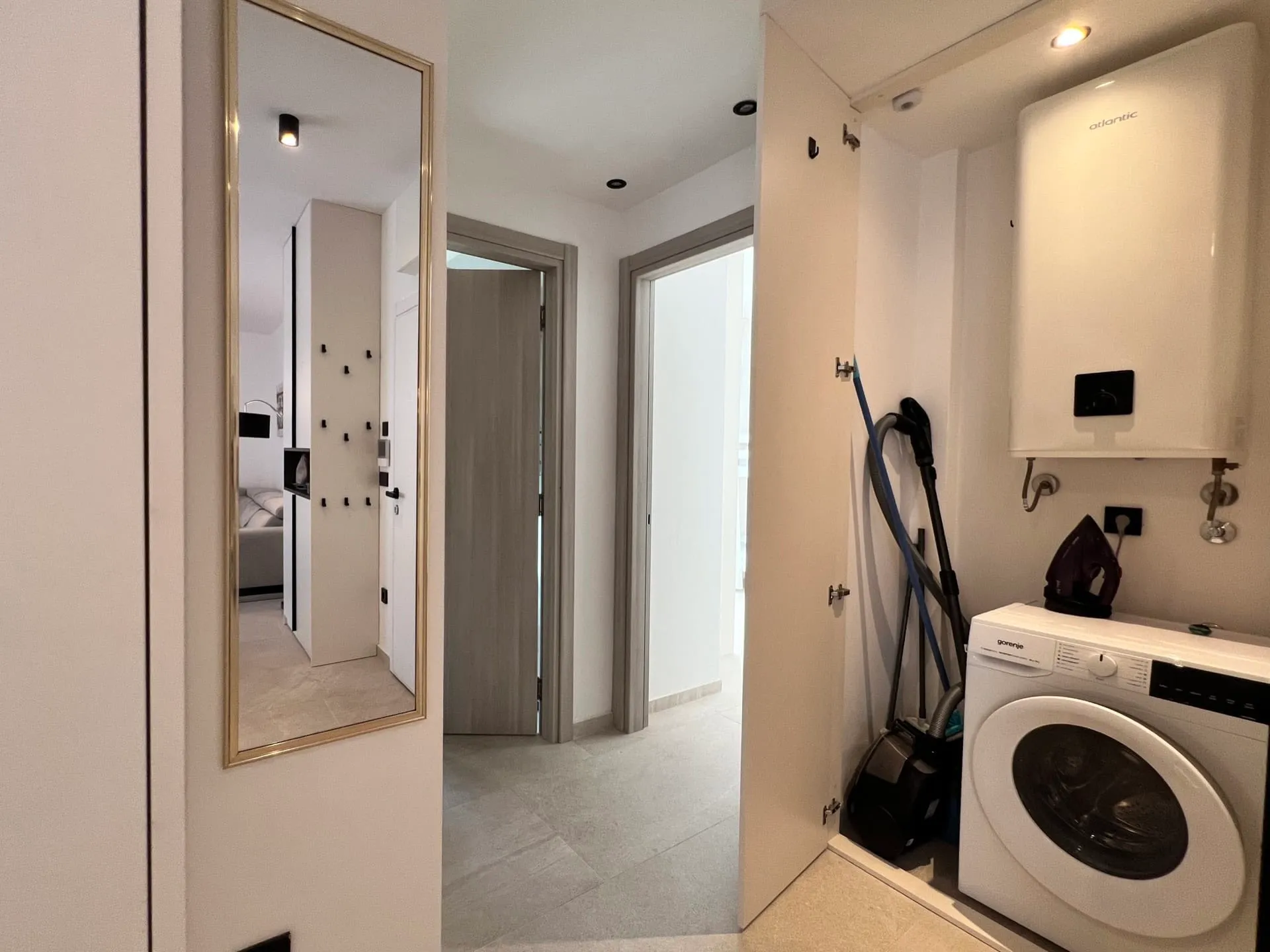 Hallway with a full-length mirror, washing machine, boiler, and vacuum cleaner in a closet.