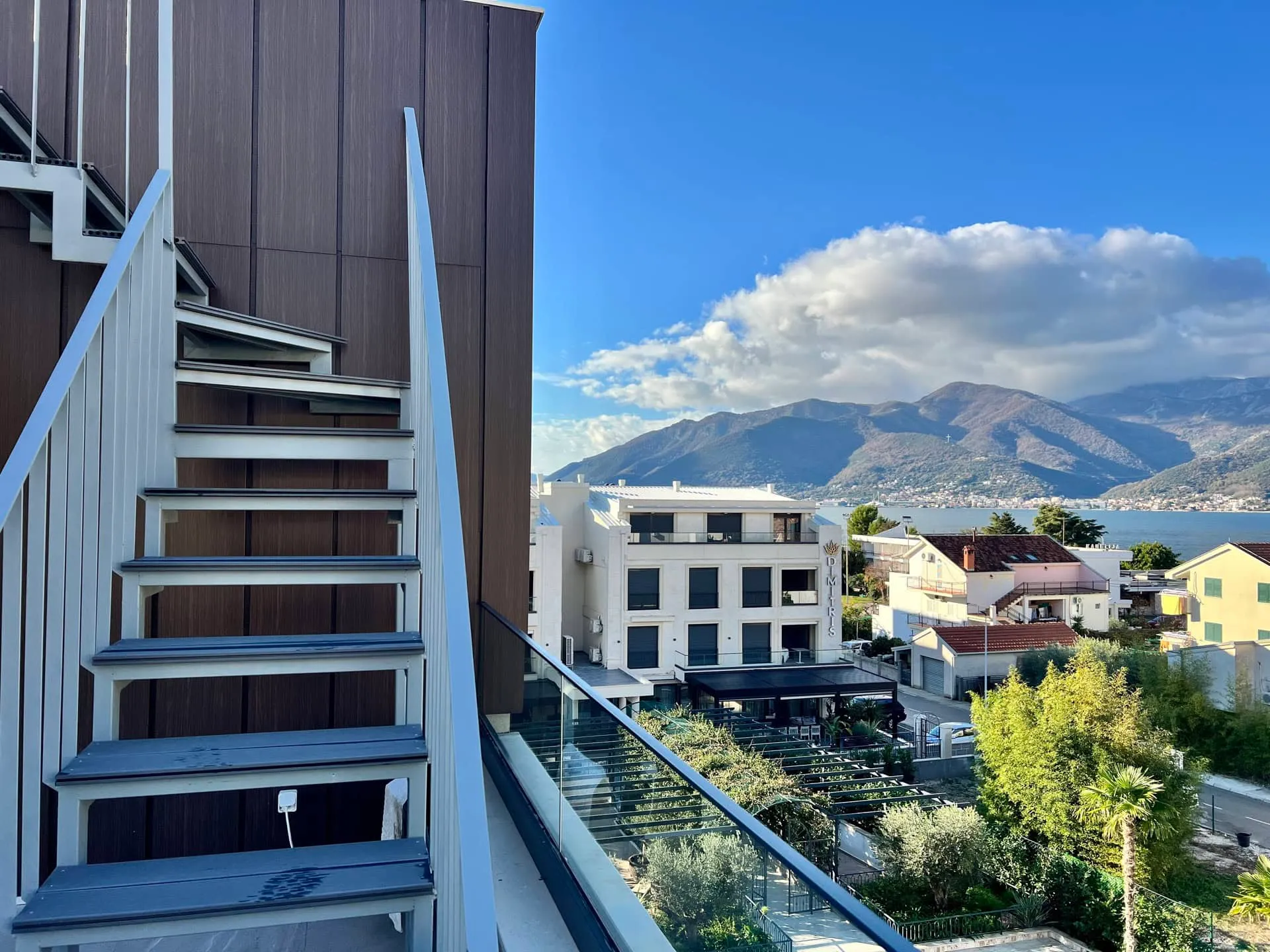 Building exterior with stairs and balcony overlooking the sea and mountains.
