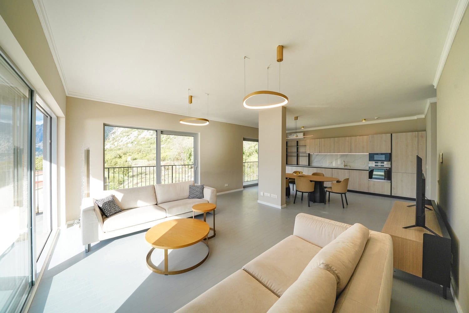 Modern living room with kitchen in an apartment, Dobrota, Montenegro: bright interior, panoramic windows, and mountain view.