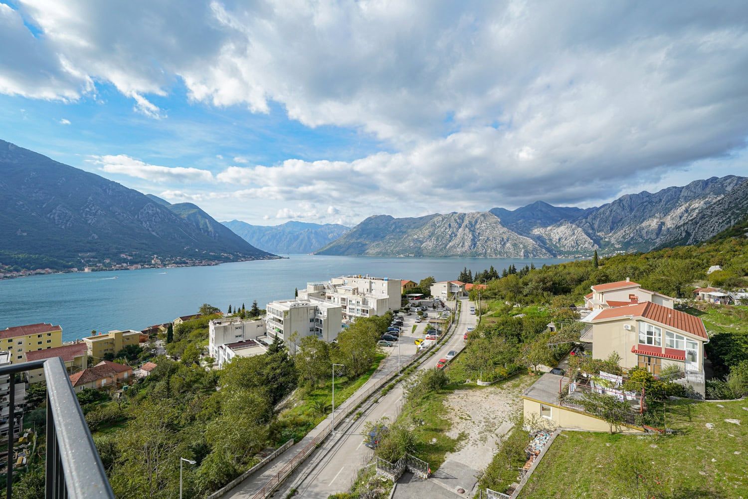 Panoramic view of the Bay of Kotor and mountains from an apartment in Dobrota, Montenegro: residential area, road, and seascape.