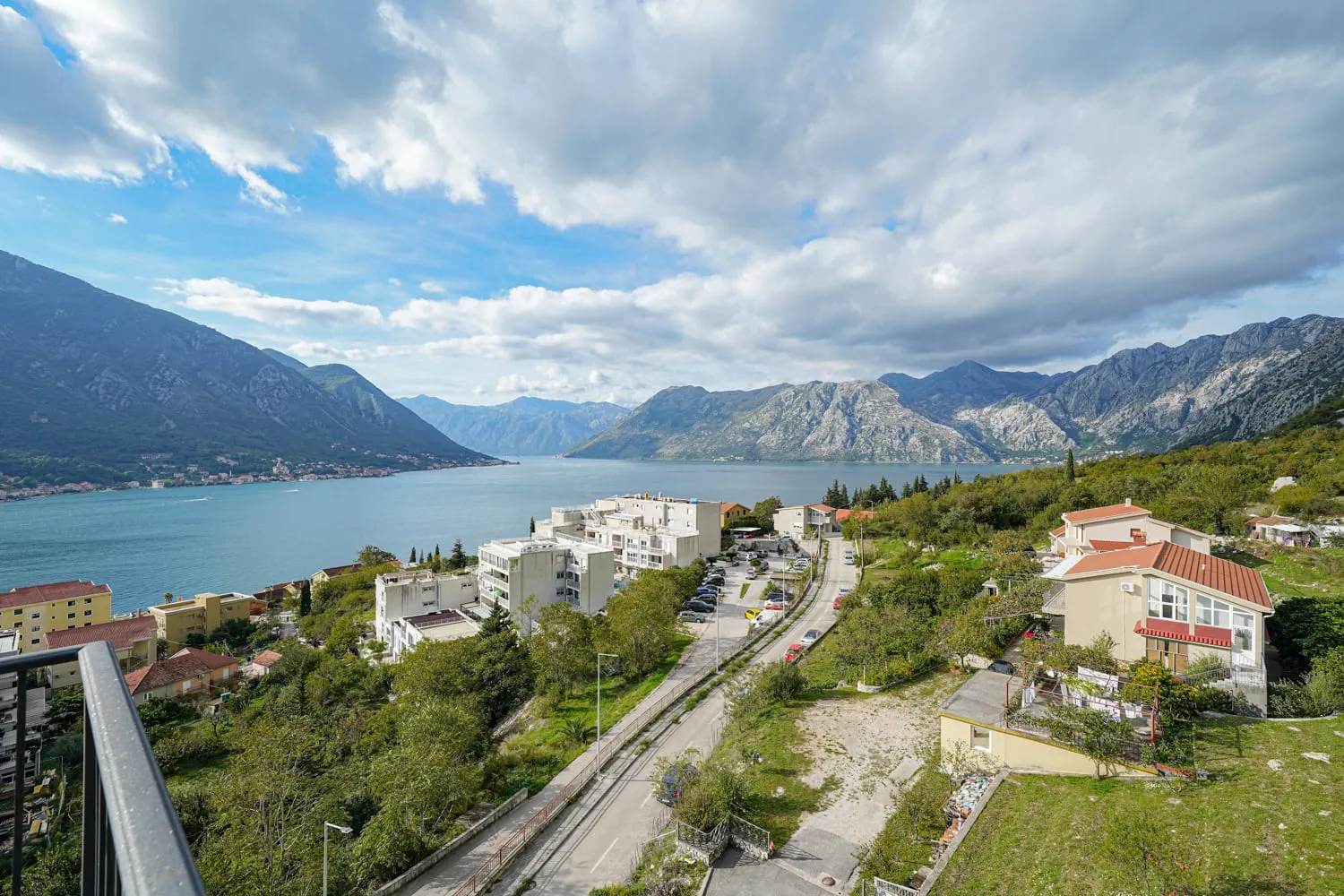 View from a balcony overlooking a bay, mountains, and residential buildings under cloudy skies.