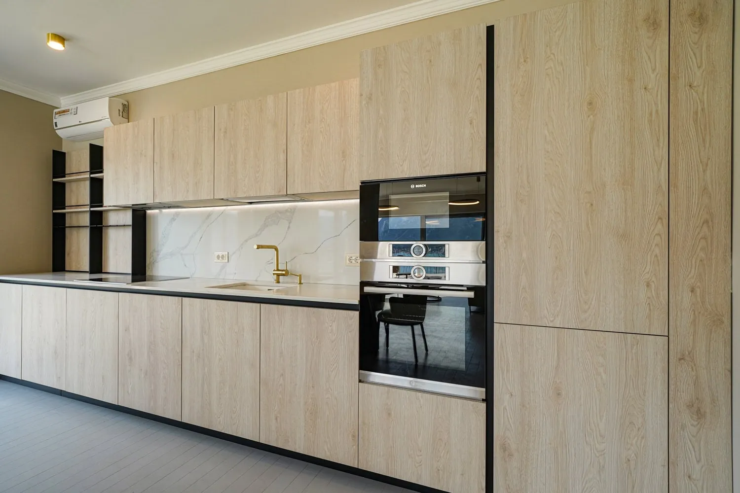 Modern kitchen featuring light wood cabinetry, built-in Bosch appliances, a gold faucet, and a white marble backsplash.