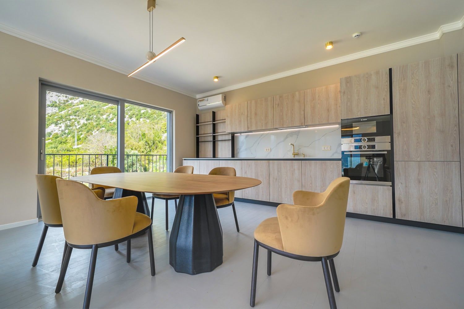 Modern kitchen with dining area in an apartment, Dobrota, Montenegro: light-colored furniture, mountain view, and panoramic windows.