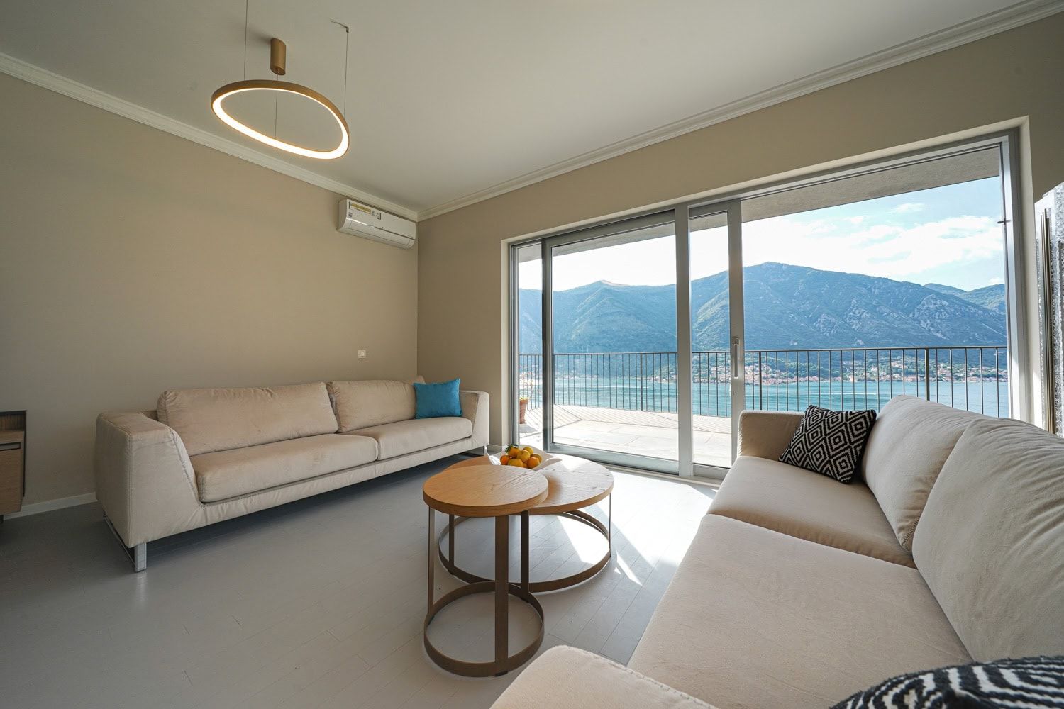 Living room in an apartment in Dobrota, Montenegro: light furniture, panoramic windows with sea and mountain views, terrace.