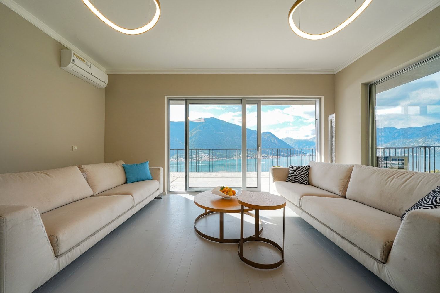 Modern living room with a view of Kotor Bay in an apartment, Dobrota, Montenegro: light-colored sofas and panoramic windows.
