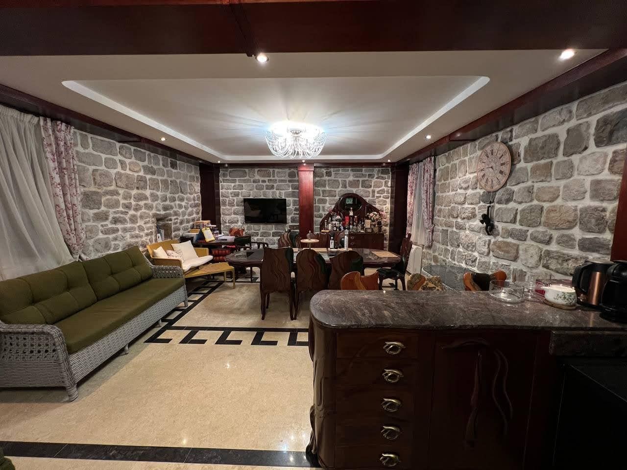 Living room with stone walls, green sofa, dining table, and bar counter under a chandelier.