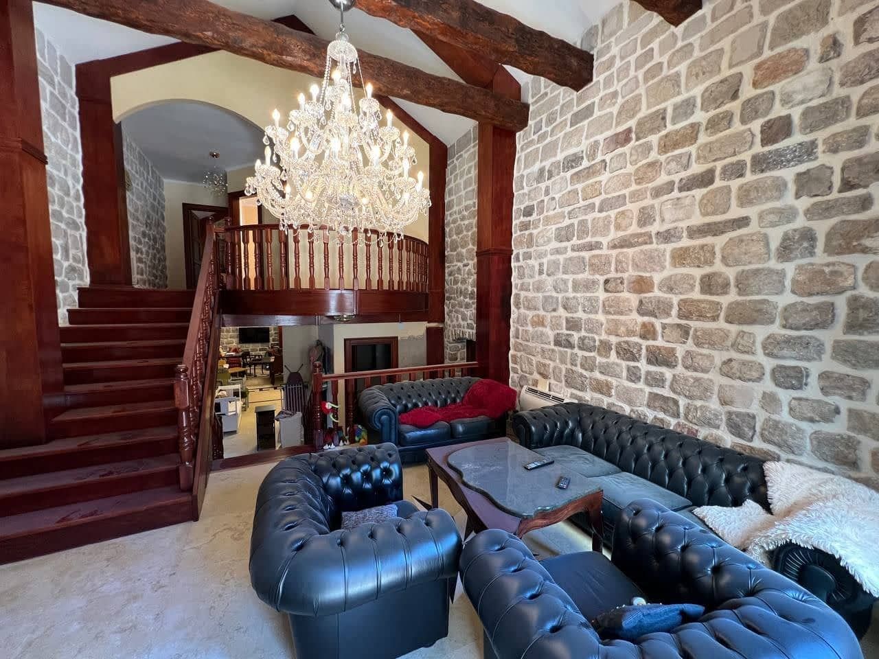 Villa living room in Kamenari, Montenegro: stone walls, wooden beams, a crystal chandelier, and Chester leather furniture.