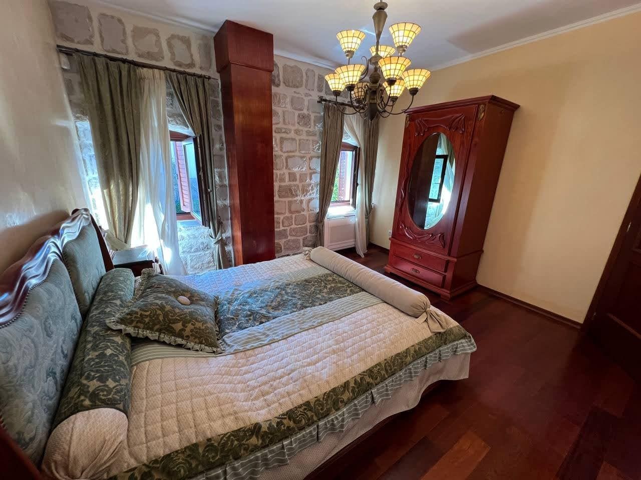 Bedroom in a villa in Kamenari, Montenegro: stone walls, antique furniture, a double bed, and a chandelier.