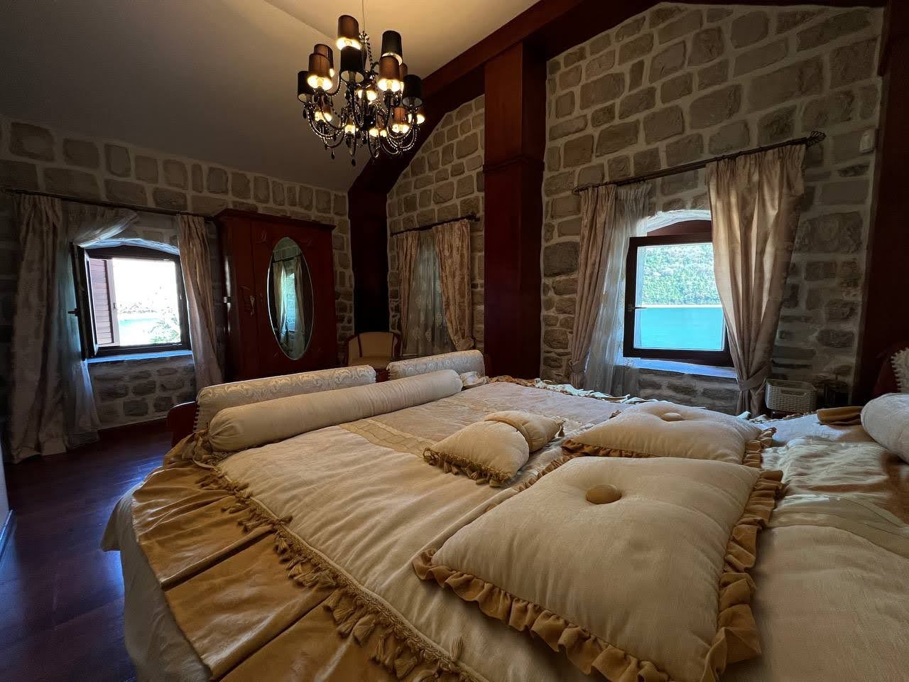 Bedroom in a villa in Kamenari, Montenegro: stone walls, a double bed, antique furniture, and a sea view.