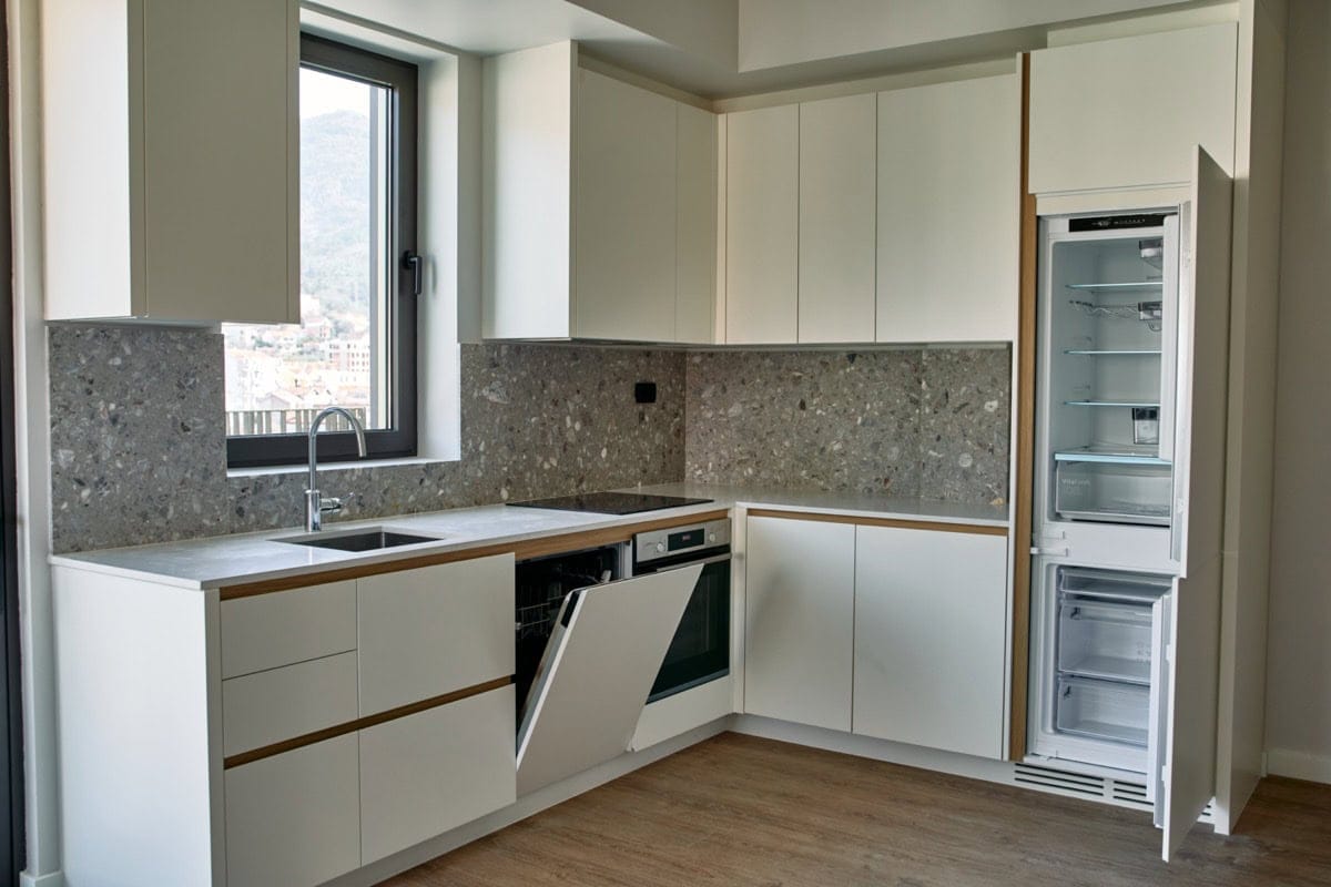 Modern white kitchen with a stone backsplash and built-in appliances in an apartment in Tivat, Montenegro.