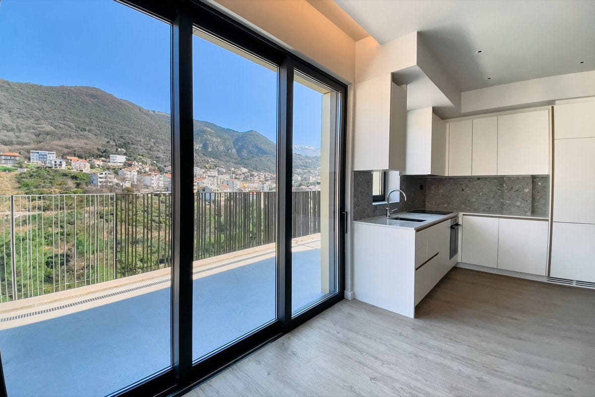 Modern kitchen in an apartment in Tivat, Montenegro, with panoramic windows and views of the mountains and terrace.