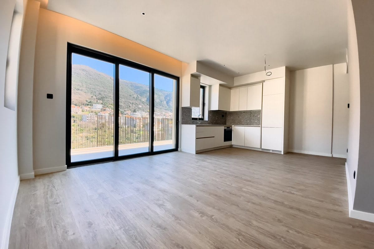 Modern living room with kitchen in an apartment in Tivat, Montenegro: panoramic windows, mountain view, light finishes.
