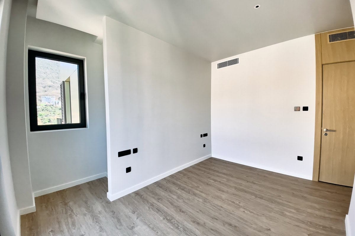 Bright bedroom with laminate flooring and mountain views in a new apartment in Tivat, Montenegro. Modern finishes and interior.