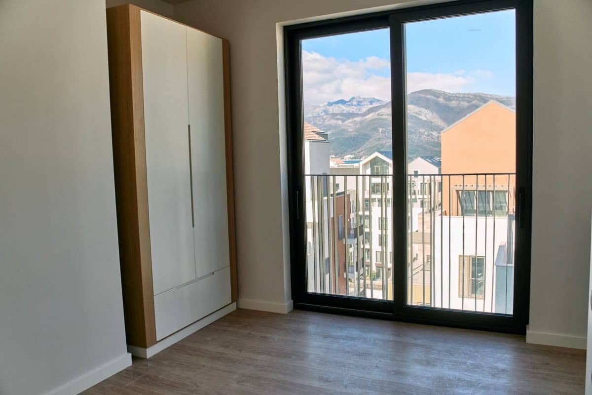 Bedroom in an apartment in Tivat, Montenegro: built-in wardrobe, panoramic window with mountain views, and a modern residential complex.