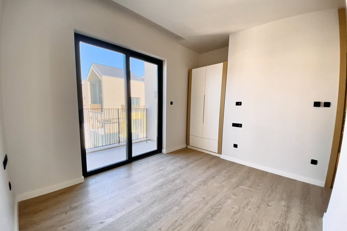 Bright bedroom in an apartment in Tivat, Montenegro: panoramic window, access to the balcony, built-in wardrobe, and laminate flooring.