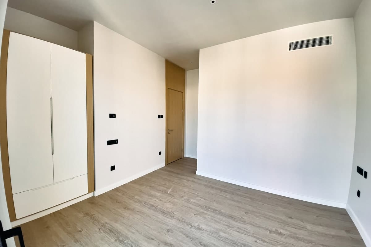 Bright bedroom with a white wardrobe and laminate flooring in a new apartment in Tivat, Montenegro. Modern finishes and air conditioning.