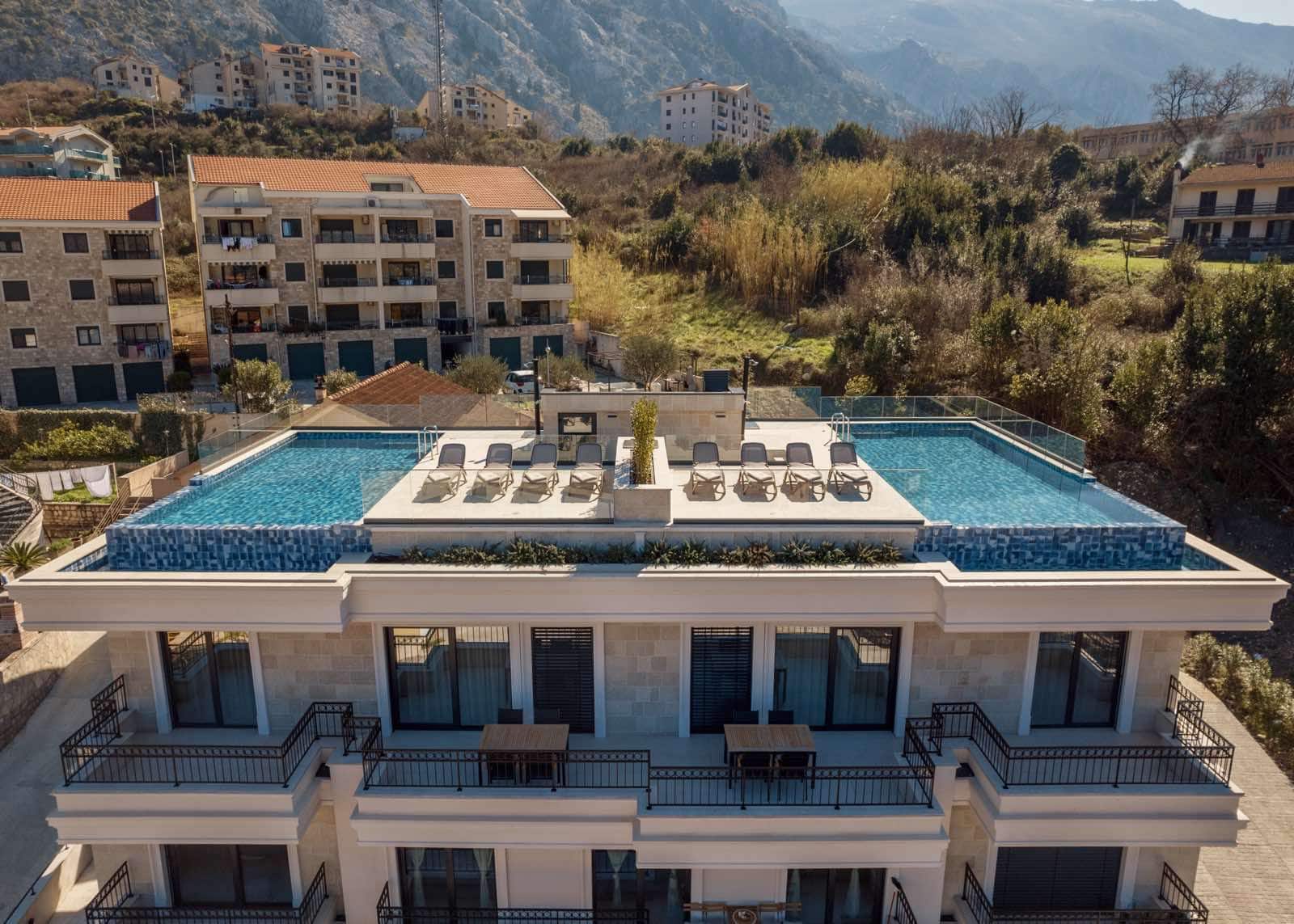 View of a residential complex in Dobrota, Montenegro, with an outdoor rooftop pool, sun loungers, and furnished terraces.