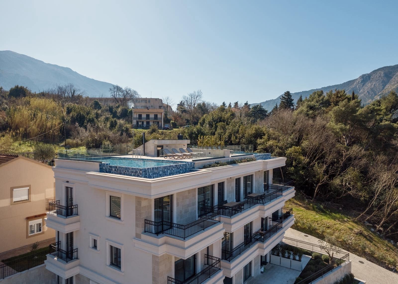 Modern villa in Dobrota, Montenegro: view of the building with a rooftop pool, terraces, and mountain scenery.