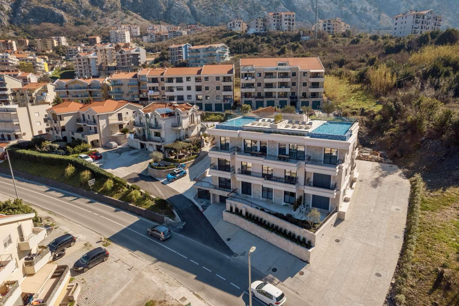 Modern residential complex with a rooftop pool in Dobrota, Montenegro: aerial view of the building and surrounding area.