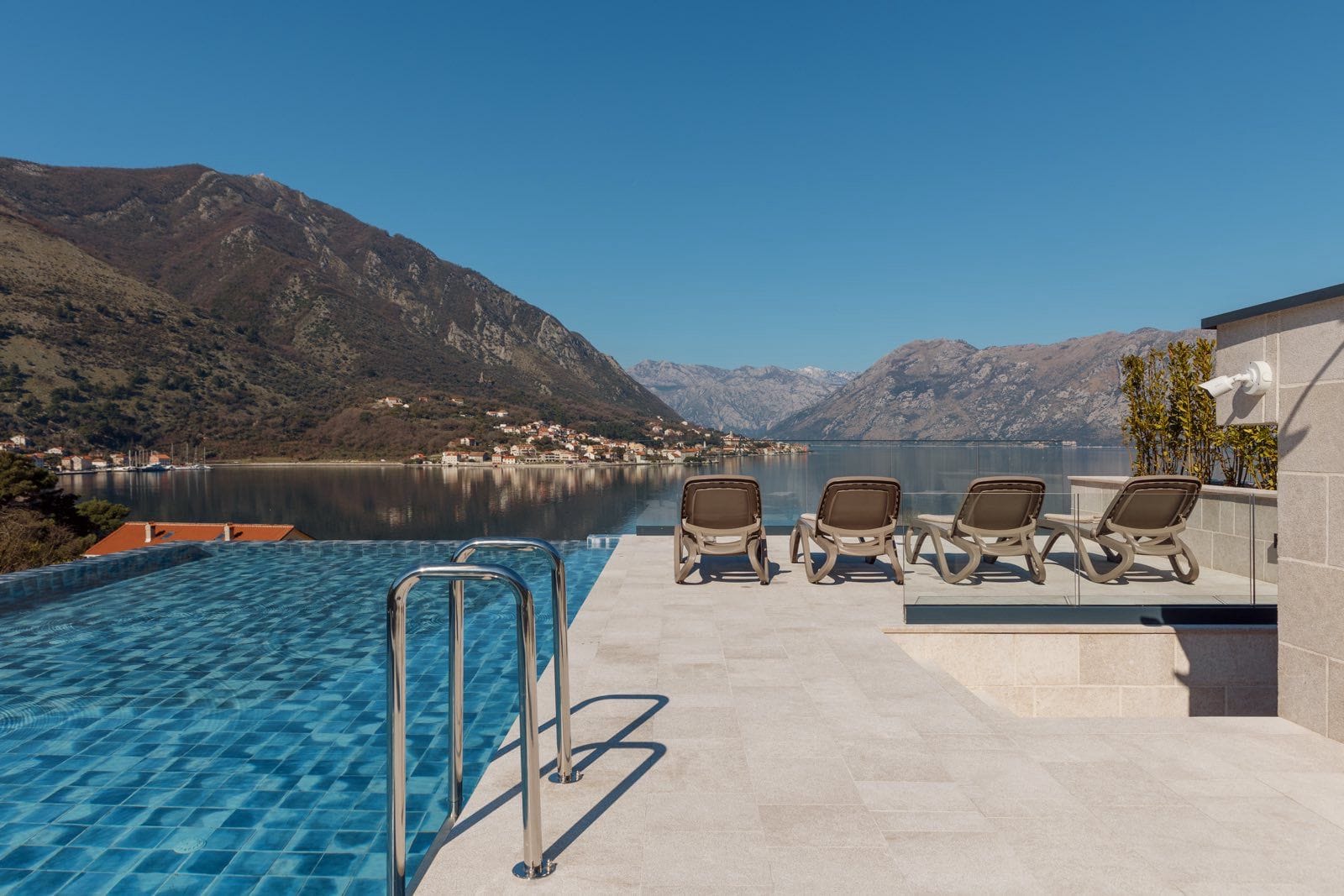 Infinity pool with views of Kotor Bay and the mountains in Dobrota, Montenegro, terrace with sun loungers by apartment No. 2412.