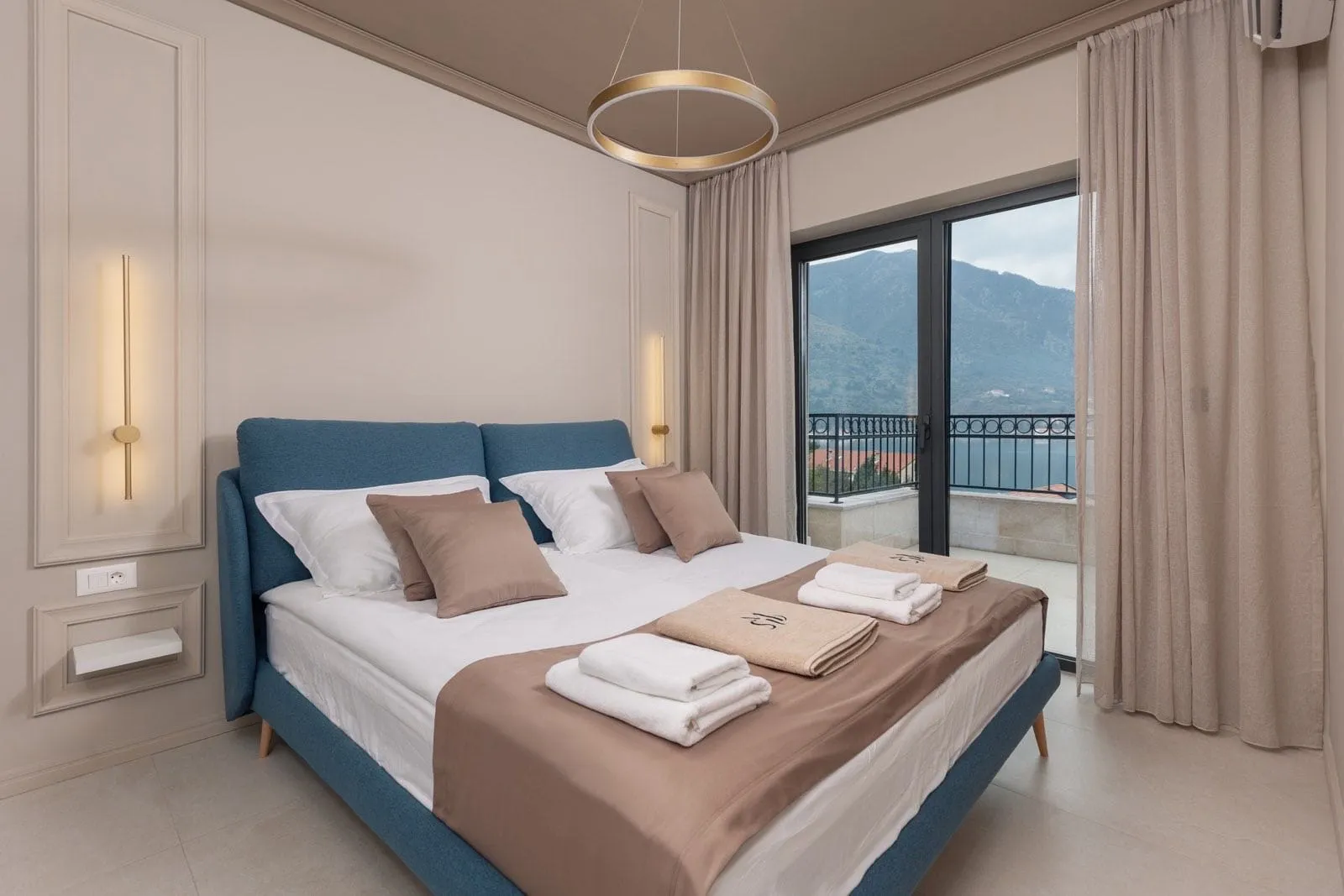 Modern bedroom featuring a blue bed frame, white linens, folded towels, and a mountain view.