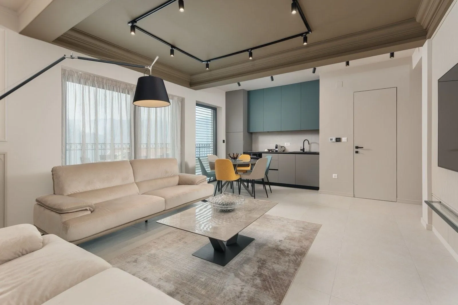 Bright living room with a beige sofa, coffee table, and an open kitchen visible in the background.