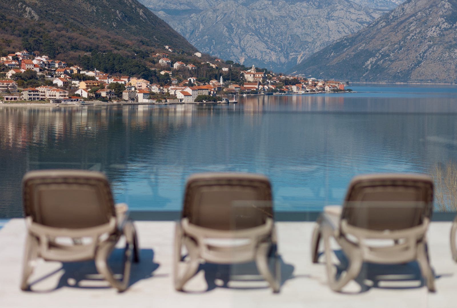 Sun loungers by the pool with panoramic views of Kotor Bay and the town of Dobrota, Montenegro.